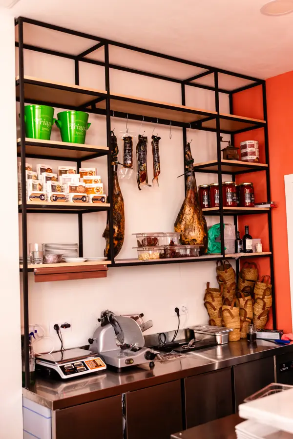 Estantería de la barra de Taberna Quimera con chacinas colgadas, jamón y cortadora