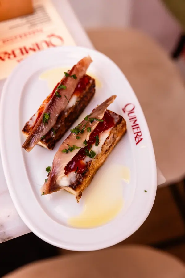 Tostas de anchoa en un plato con el logo de Quimera