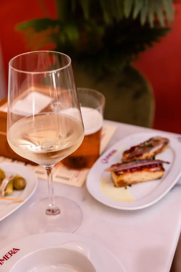 Copa de vino blanco, caña y tosta de anchoa en una mesa de Taberna Quimera